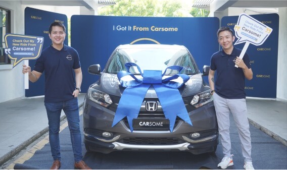 Para pendiri yang memegang mobil papan nama mobil dengan mobil yang dibungkus pita biru di antaranya